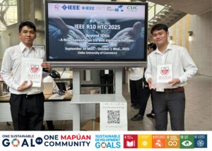 Two people at ieee r10 htc 2025 event holding mapúa bags screen displaying conference details at chiba university