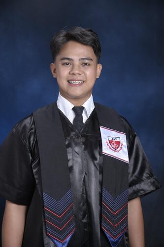 Smiling graduate in a black gown with a crest posed against a dark blue background