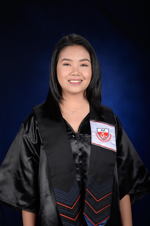 Graduate in black gown with emblem smiles against a dark blue background