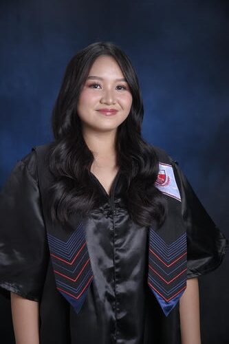 Young woman in graduation gown with long hair smiling against a dark blue background