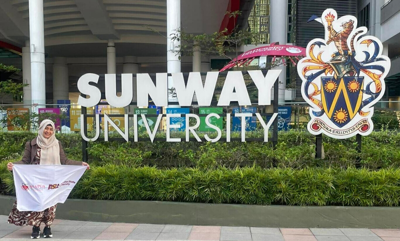 Person holding a banner stands by sunway university entrance showcasing logos and colorful background signs
